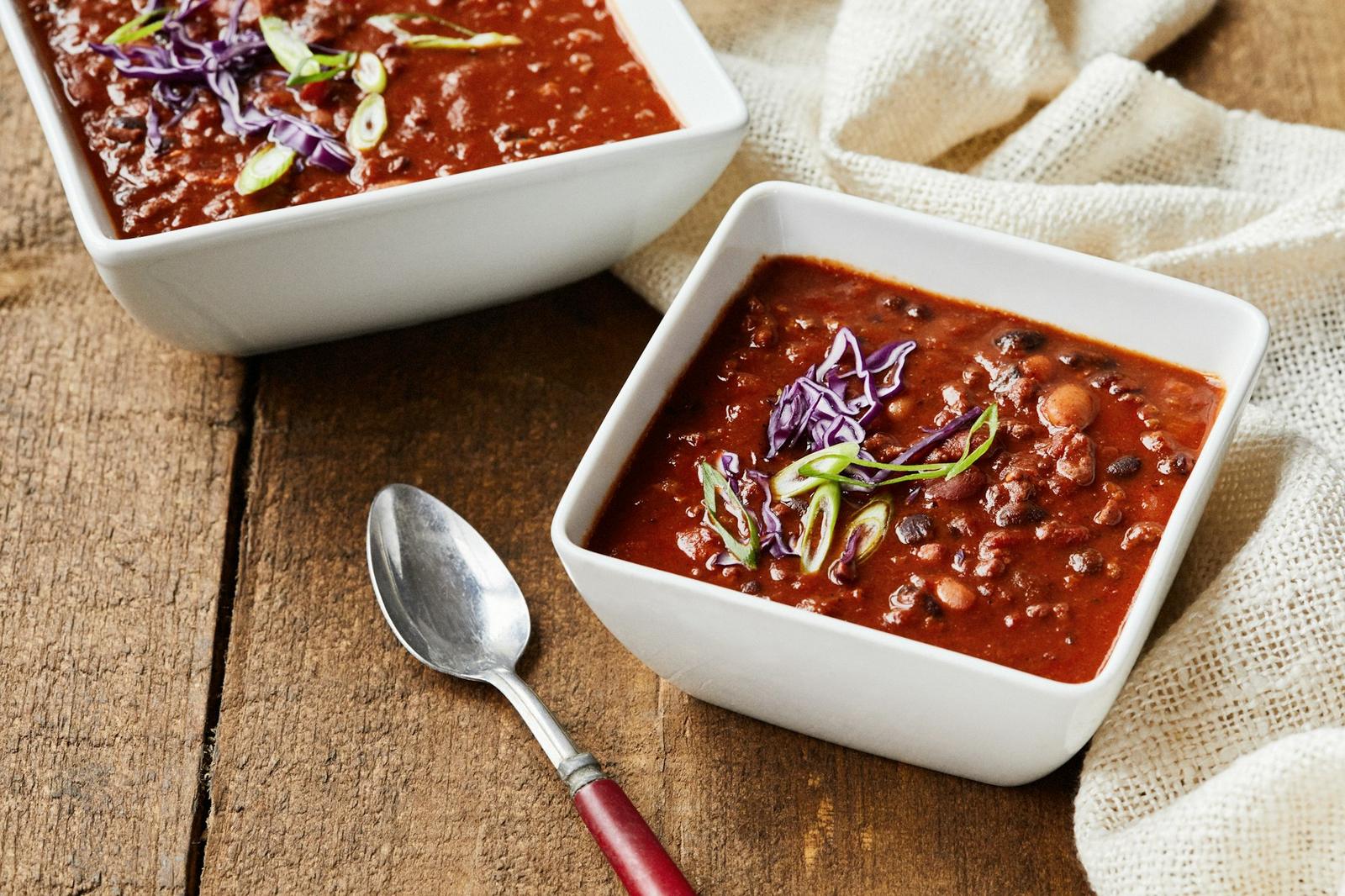 Two bowls of homemade chili with a spoon on a rustic wooden table